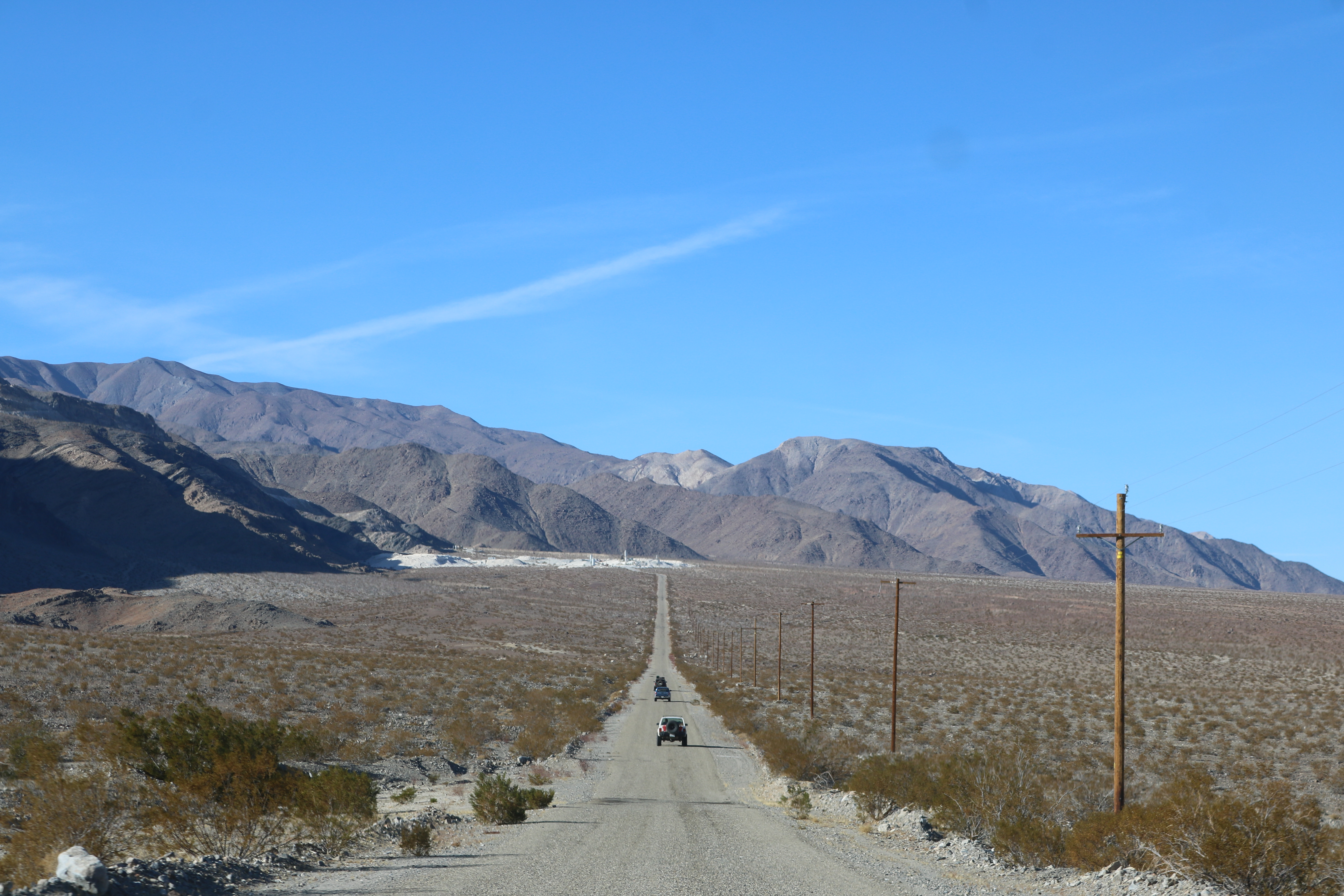 A white XJ, a blue Tacoma, and a green XJ on a long paved road with a working mine in the background.