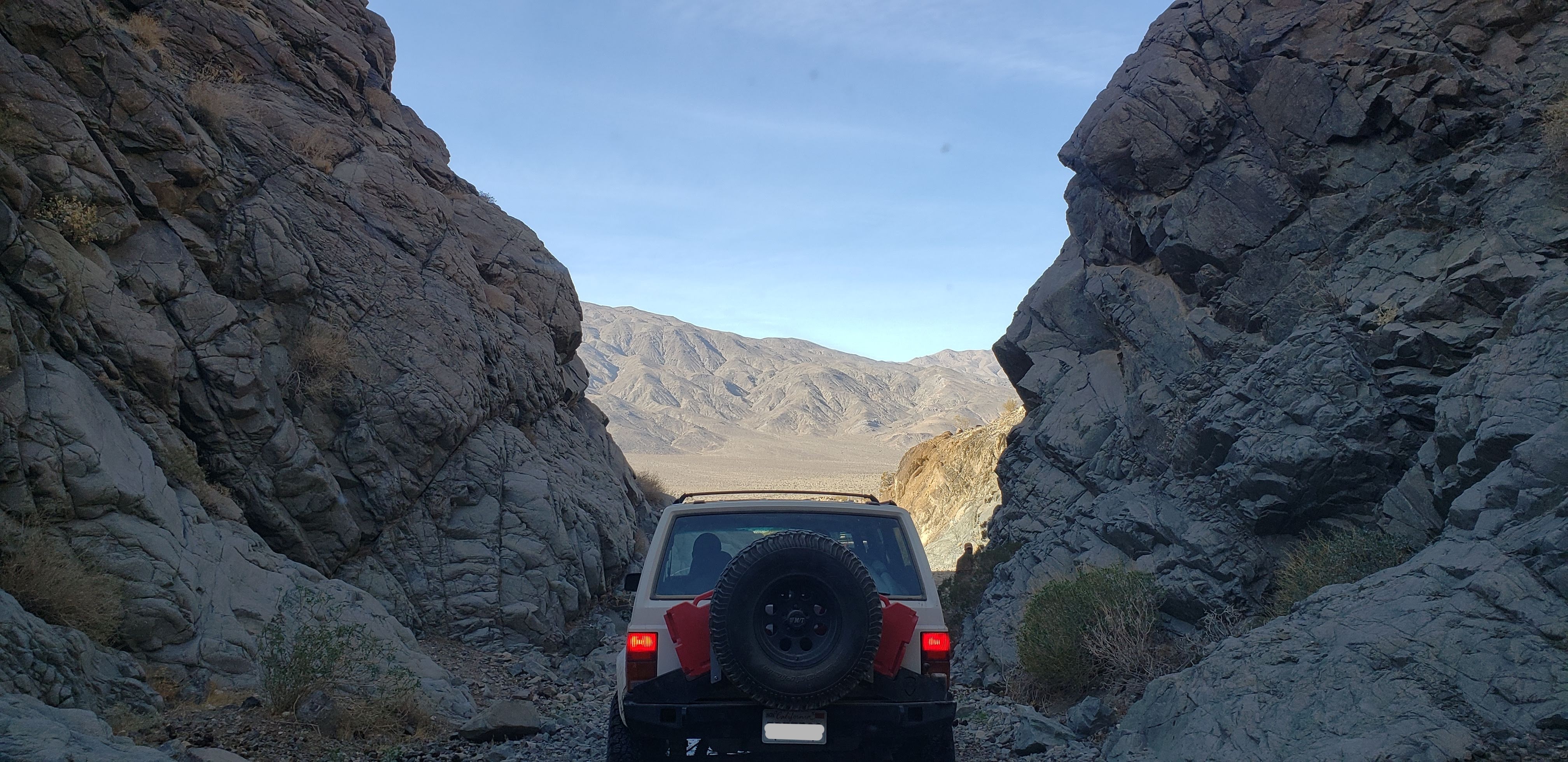 The back of a white Jeep XJ driving out of a slot canyon.