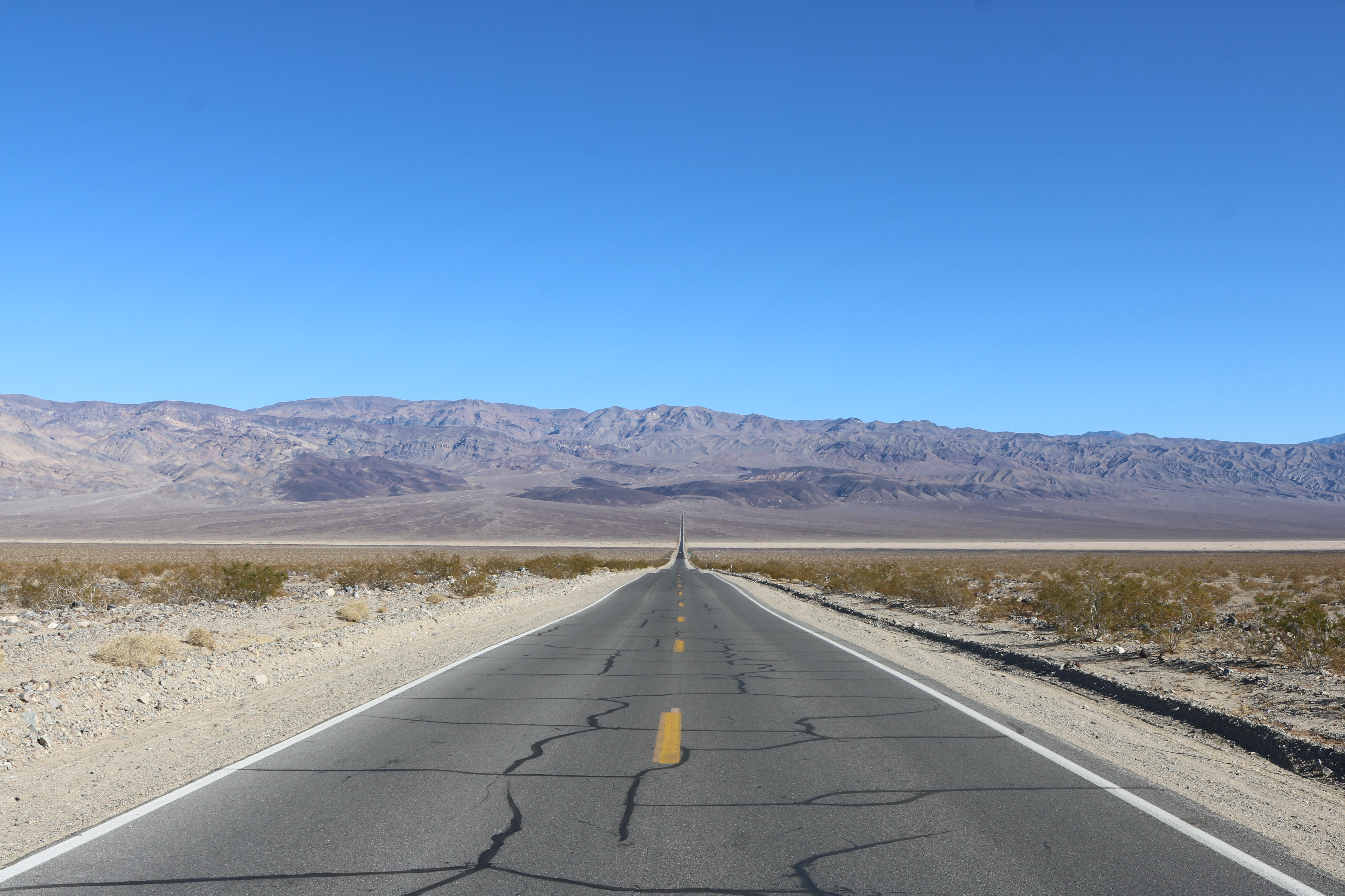 A long two lane highway fading away into the mountains in the background.