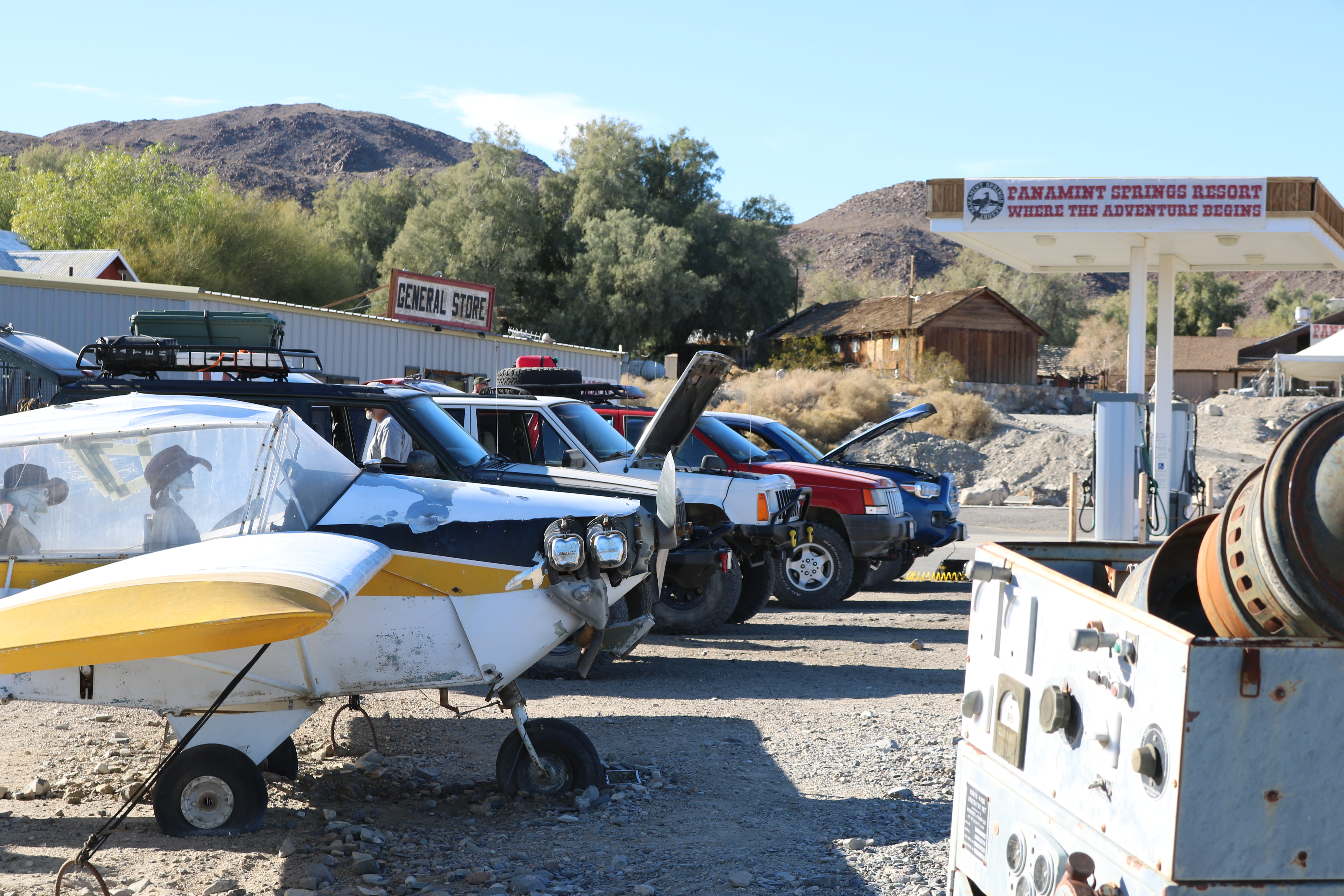 An airplane with skeletons in the seats in front of a green ZJ, white XJ, red ZJ, and blue Tacoma at a gas station.