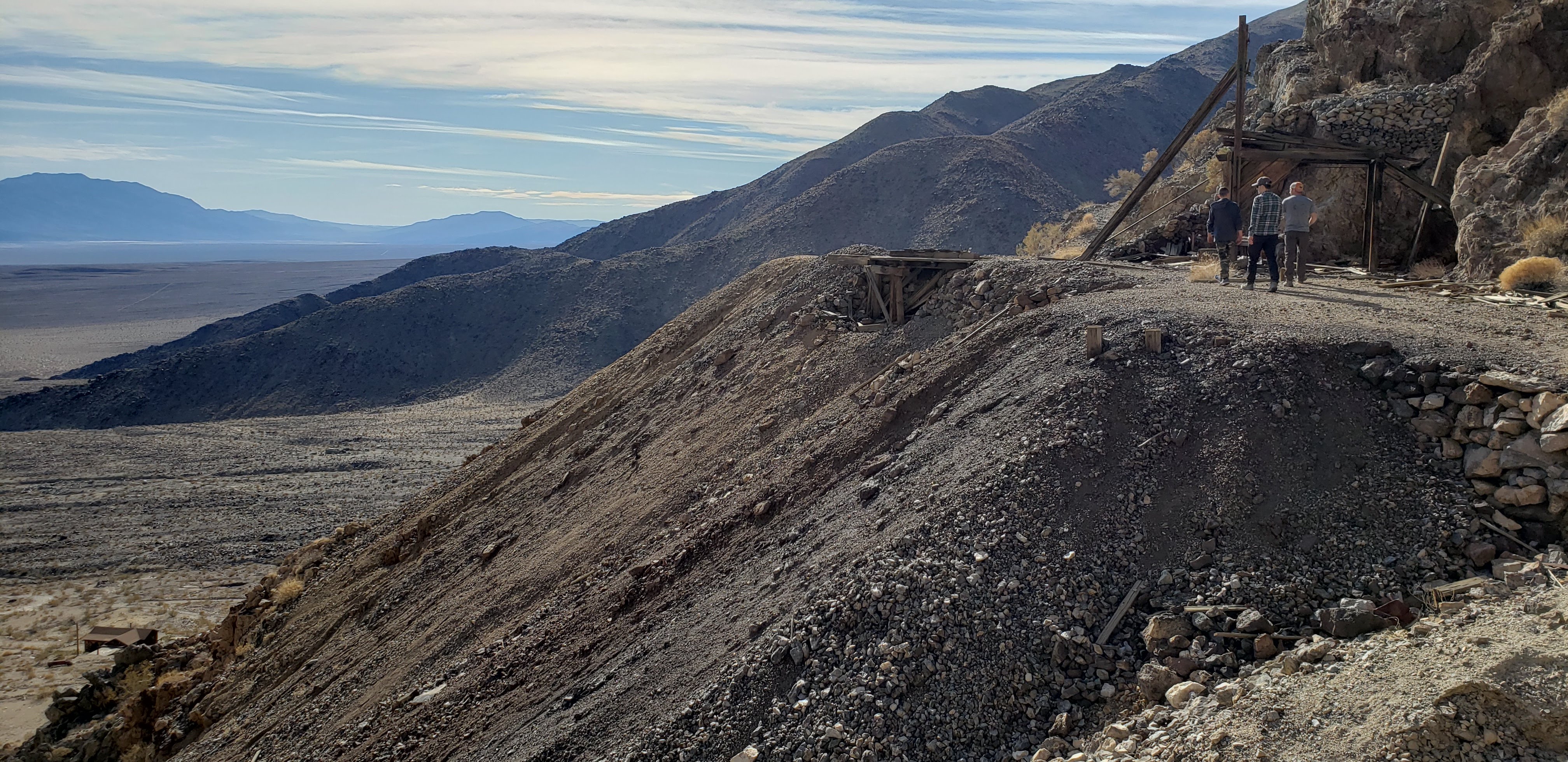 Three men walking on a pile of dirt and rocks with ruins of mining in view.
