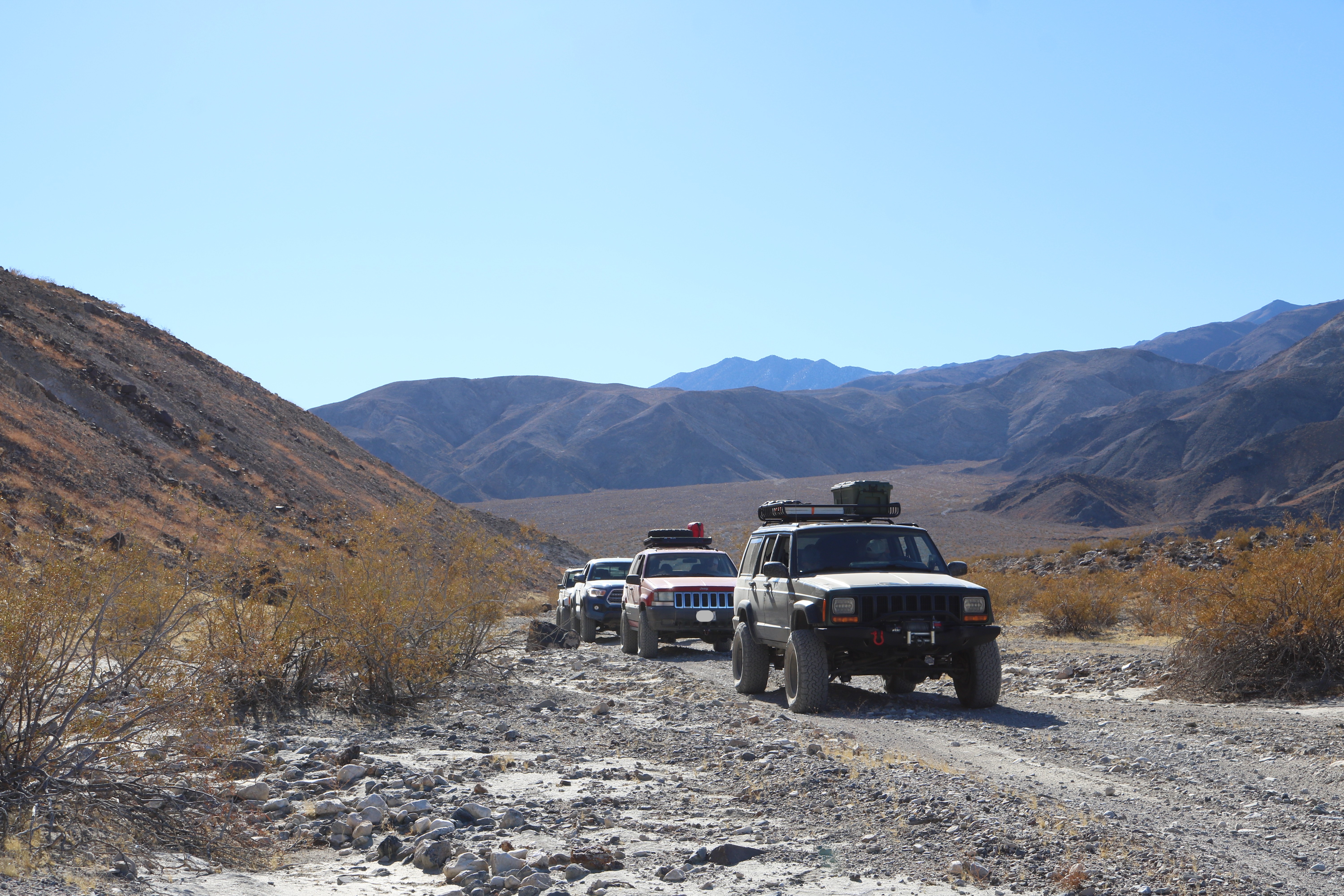 Green Jeep XJ followed by a red Jeep ZJ followed by a blue Tacoma on a dirt trail.